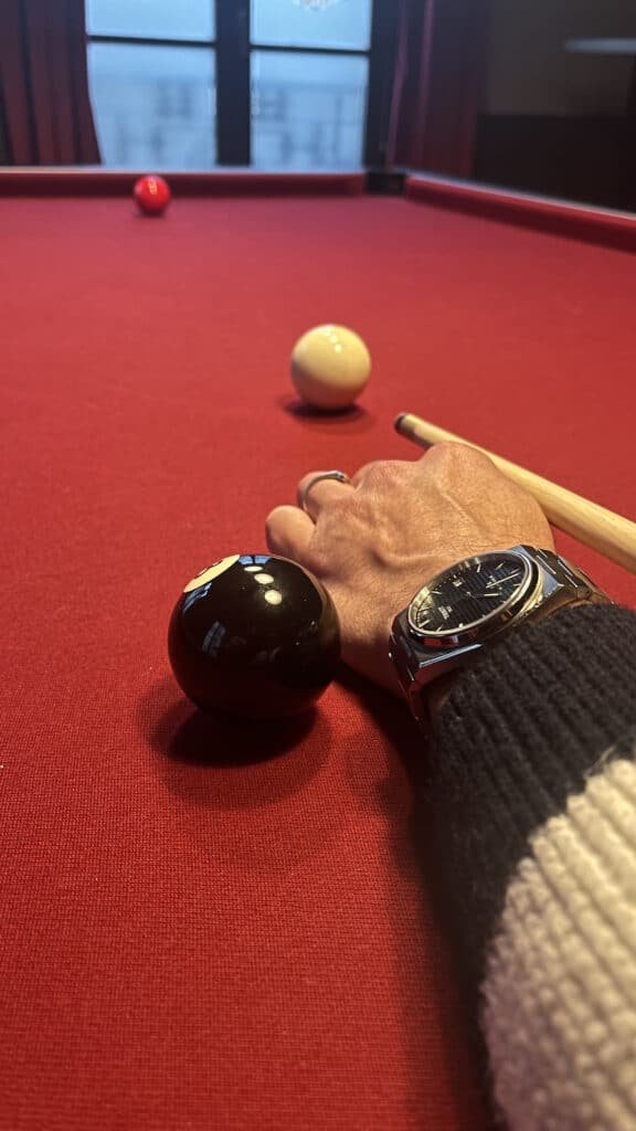 Main tenant une boule de billard noire sur une table de billard rouge à My Pub Rouen